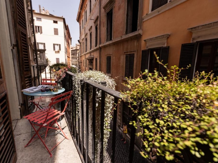 Charmanter Balkon, Rote Klappstühle, Lebendiges Grün, Städtische Architektur, Sonnige Atmosphäre